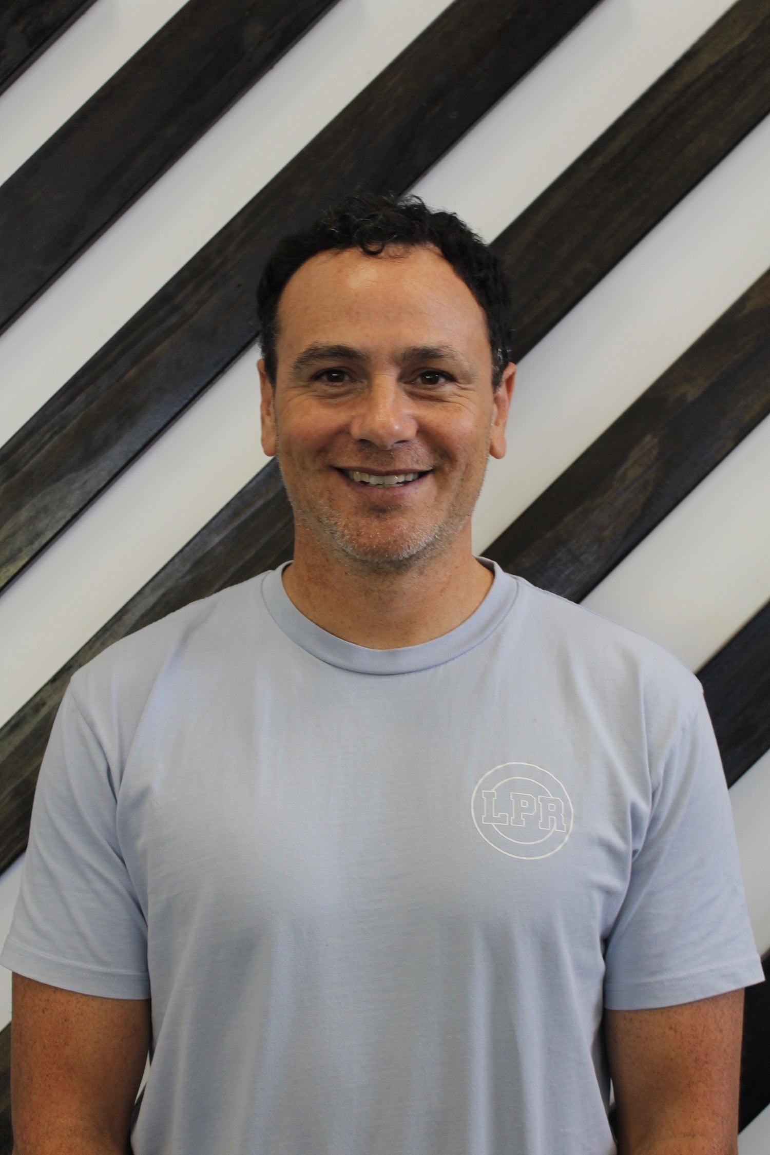 Quentin a physio at Leaton Performance standing behind a black and white striped wall.